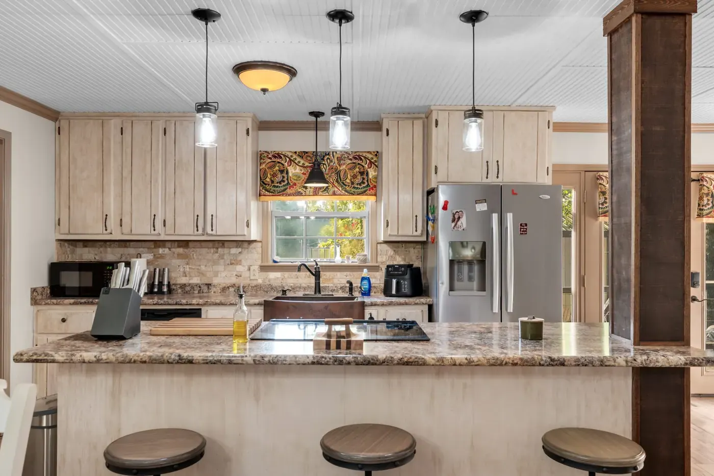Kitchen island with three bar stools and pendant lights above