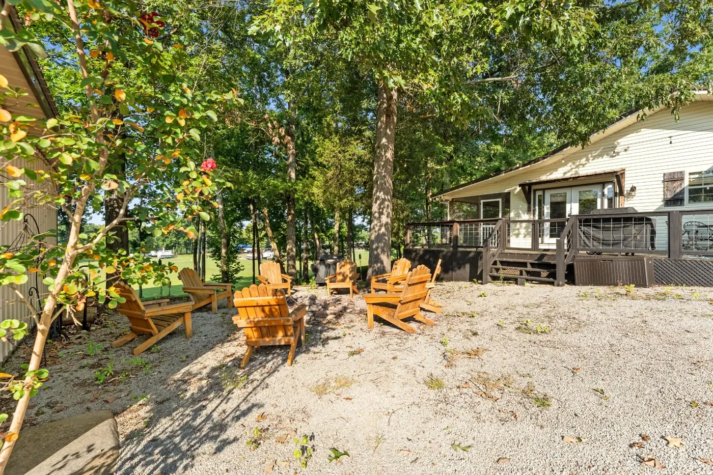 Adirondack chairs set out on the gravel under the trees behind the house