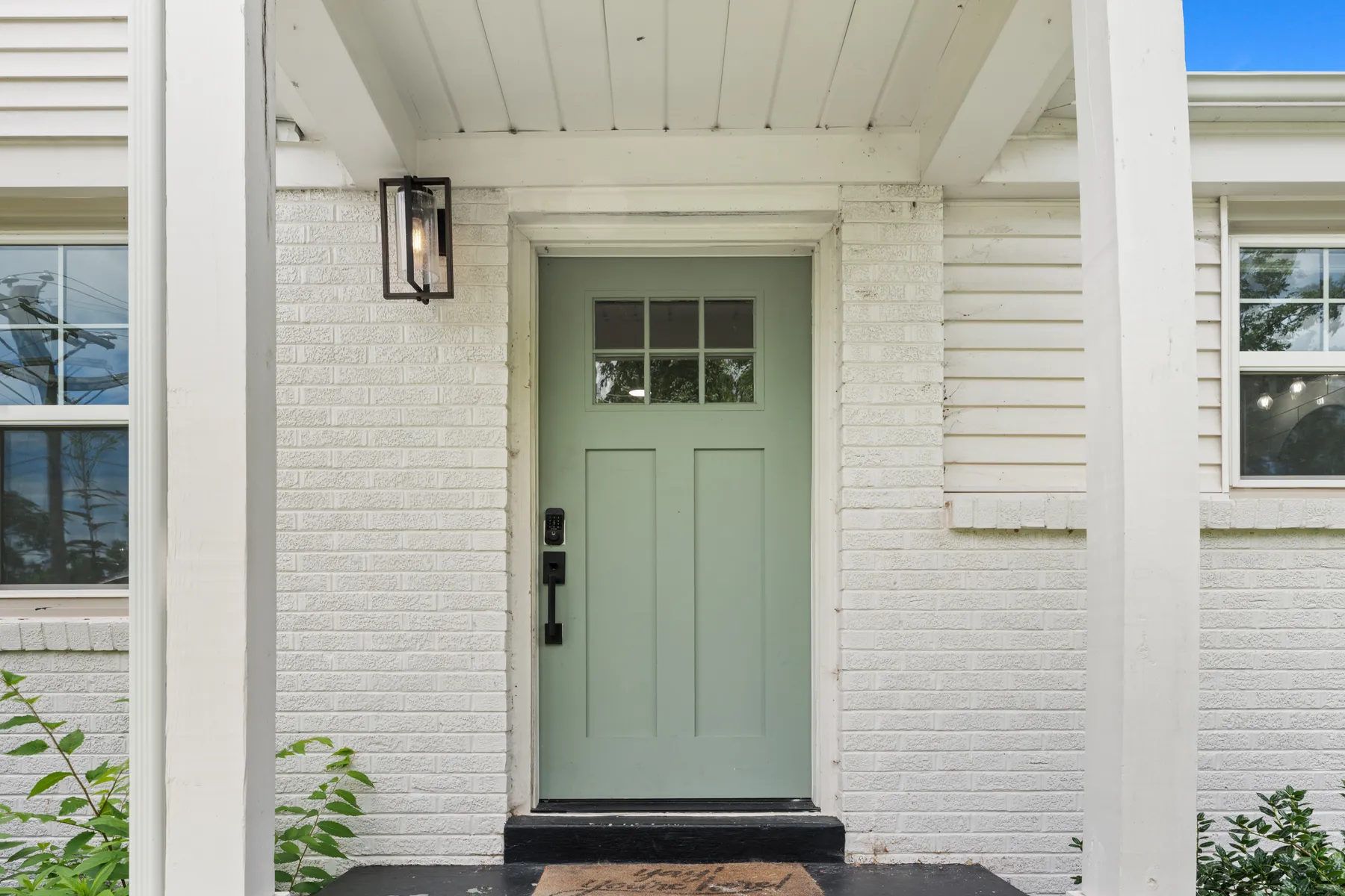 Green front door with a sconce against a brick facade