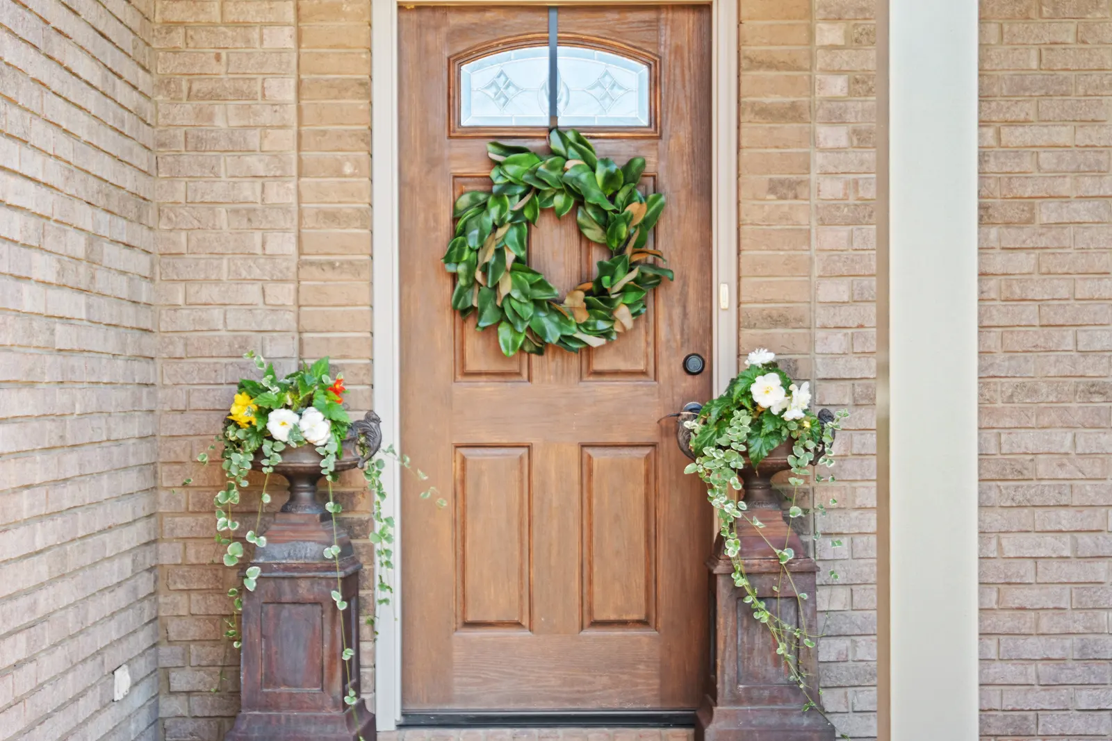 Arched wood front door with a magnolia wreath and brick surround