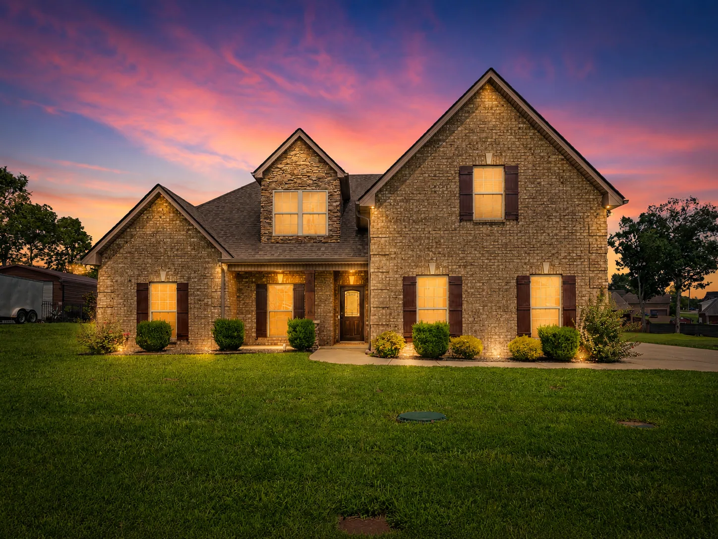 A Middle Tennessee brick home at twilight, its windows glowing warm against a dusk sky